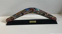 Front view of hand painted Indigenous Australian boomerang displayed on black stand with plaque