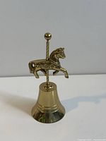 Front view of vintage brass handheld bell with a carousel horse mounted on a vertical pole topped with a ball finial.