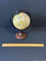 Front and side view of the vintage globe on wooden base with metal meridian rings, ruler for scale showing approximately 9 inches tall