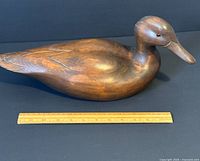 Side view of the large wooden duck decoy with ruler for scale showing 16 inches length and carved details.