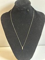 Necklace displayed on black velvet stand showing full length of thin silver chain and small pendant.