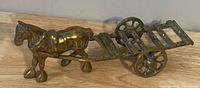 Side and angled views of a solid brass horse pulling a two-wheeled cart carriage buggy wagon model on a wooden surface