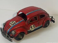 Front and side view of red vintage style metal model car with race number 53 and blue/red stripe on top.