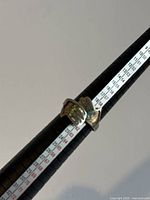 Silver ring on a ring size measuring tool showing approximate size 9 with open band and two hand shaped ends.