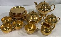 Gold lusterware teapot, sugar bowl, creamer, cups, and plates arranged together on a table showing overall items in the lot.