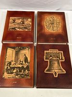 Four leather bound history books with embossed covers depicting historic American scenes including the Liberty Bell and colonial meetings