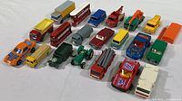 Full front view of all 20 die cast vehicles showing a variety of cars, trucks, buses, a green tractor, and army personnel carrier with an orange flatbed truck positioned on the far right.