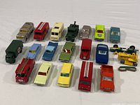 Overview photo showing all 20 die cast toy vehicles in various colors and styles including buses, fire trucks, sedans, and a green tractor with broken track