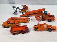 Top view of all six large die cast trucks positioned together showing orange color and details including missing wheels on one vehicle and residue on another