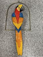 Front view of full 38-inch plastic macaw parrot perched on brass semi-circular ring
