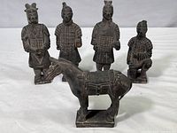 Front view showing five Terracotta Warrior figures and one horse figure arranged in a row, depicting different poses and armor details.