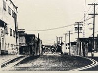 Front view of the black and white vintage framed print showing a street scene from Cannery Row, with buildings, poles, and overhead wires visible.