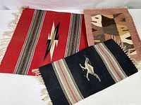 Three vintage hand woven wool textiles shown together, emphasizing the distinct designs: red geometric, black roadrunner, and pinkish fish pattern.