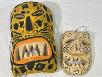 Two jaguar style wooden masks, adult and child size, showing front face with carved teeth and painted animal spots
