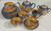 Full set showing cups, saucers, plates, teapot, creamer, and sugar bowl with lusterware glaze in blue and gold tones.