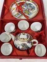 Top-down view of the tea set inside red fabric box showing teapot, six cups, and decorative plate tied with red ribbon.