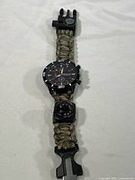 Full view of survival watch bracelet showing watch face, braided paracord wristband, compass integrated near the buckle, and black plastic buckle.