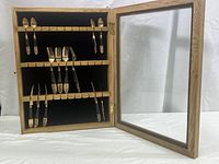 Cutlery set displayed in an open wooden frame with glass front, showing all utensils held in place inside