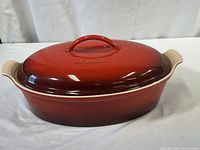 Full view of the Le Creuset oval dish with lid, showing cerise color, integrated handles, and glossy finish.