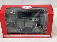Black 1:24 diecast model car in original red Coca-Cola branded box with clear front window, showing details of the vehicle and packaging.