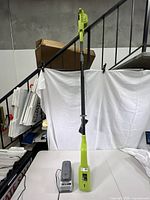 Full view of the cordless pole chainsaw standing upright with no blade attached, showing green and black colors and telescoping pole.