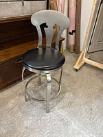 Full view of bar stool showing metal frame, black seat and curved backrest