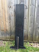 Full view of tall black wooden shelf standing against fence