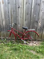 Full view left side of red Raleigh bicycle against wooden fence
