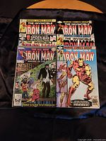 Six Iron Man comic books arranged on a black cloth, showing the front covers.