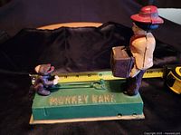 Front view showing man figure holding suitcase and monkey figure on green base with embossed 'MONKEY BANK'