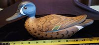 Side view of the hand carved wooden duck decoy showing detailed feather carvings and paint including green wing patch and blue head with white stripe.