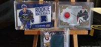 Front of three NHL hockey cards showing rookie materials patch, player photos, and memorabilia fabric swatches.