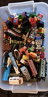 Bin filled with a variety of small toy cars and trains, various colors and styles visible