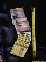 Large stack of Pokémon trading cards displayed alongside a measuring tape showing approximately 10 inches in length.