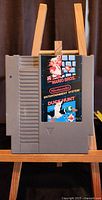 Gray NES cartridge with colorful Super Mario Bros and Duck Hunt label on front showing classic pixel art characters and title.