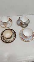 Four antique English bone china teacups each paired with their individual saucers, shown on a white surface