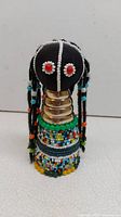 Front view of the African decorative beaded doll showing black fabric head with red and white beaded eyes, metal coil neck rings, and multicolored beaded torso.