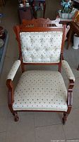 Front view of antique wooden armchair showing upholstered seat and back with diamond pattern, carved wood frame and armrests.