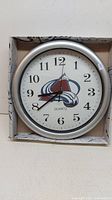 Front view of the round wall clock with Colorado Avalanche logo in box.