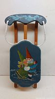 Front view of wooden sled showing the painted gnome design and attached white rope handle.
