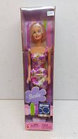 Front view of boxed Barbie Cares Doll by Mattel with floral dress and purple background packaging