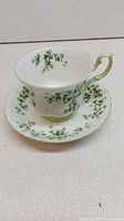 Cup and saucer displayed together showing shamrock pattern and green handle on cup.