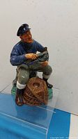 Front side view of Royal Doulton figurine depicting a seated man holding a lobster next to a lobster trap basket.