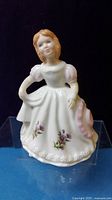 Front view of Royal Doulton porcelain figurine depicting young woman in white dress with floral decoration and pink accents