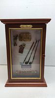 Front view of the wooden display case with glass door showing golf-themed miniatures inside including three golf clubs, golf bag, trophy and golf cart model, with a plaque above the display reading 'Old Chest'
