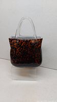 Front view of tortoiseshell pattern animal print glass handbag decoration with clear handles placed on a white surface.