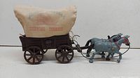 Side view of metal wagon with cream canvas cover labeled 'Patent Applied For Chewing Tobacco' and two grey metal horses attached.