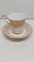 Porcelain teacup and saucer with gold filigree design viewed from front, showing elegant pattern and shape