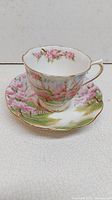 Porcelain teacup and matching saucer set with hand-painted pink floral design and gold trim, showing overall aesthetic and condition.
