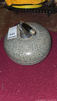 Top view of the curling stone showing speckled granite surface and attached metal handle with black grips.